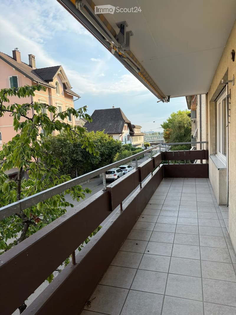 Balcony with tiled floor, wooden railing, and view of street and surrounding buildings.