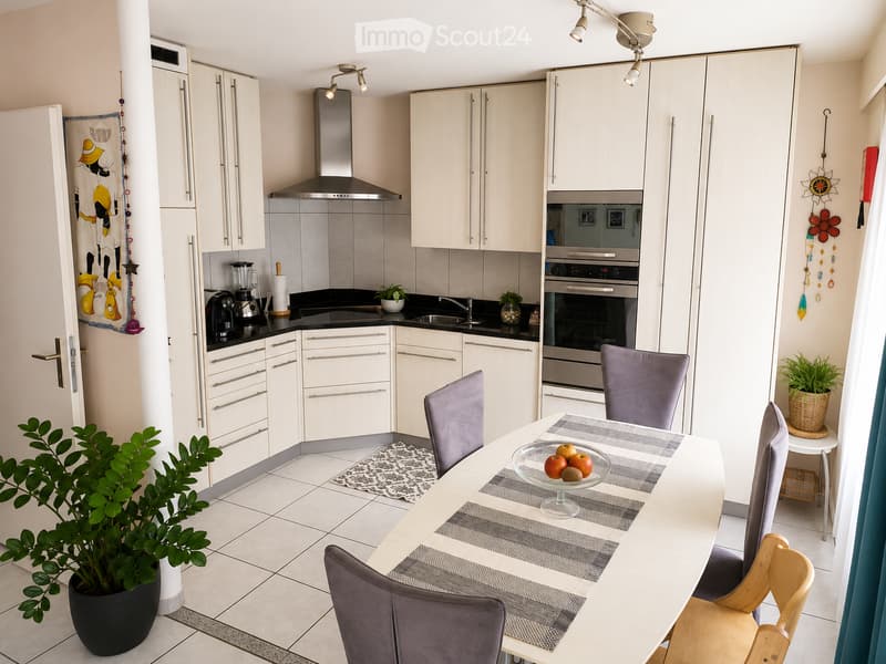 Modern kitchen with white cabinets, stainless steel appliances, a dining table with chairs, and decorative plants.