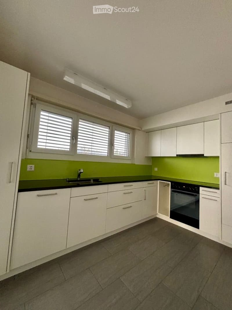 Modern kitchen with white cabinets, green backsplash, black countertop, and stainless steel sink and oven.