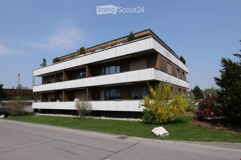 3 story building, white and brown exterior, multiple balconies, windows, green lawn, trees