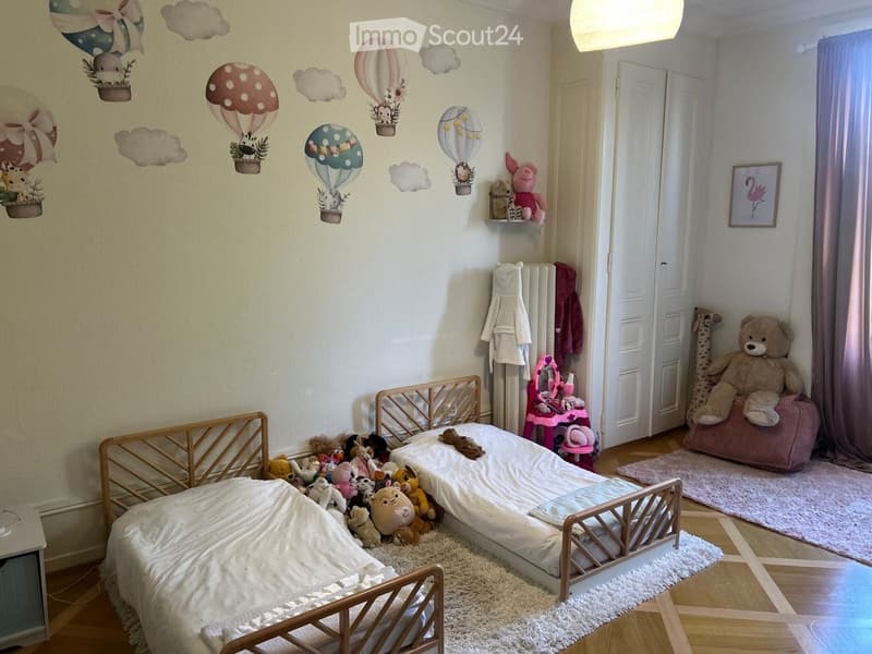 A child’s bedroom with a small bed, stuffed toys, a pink chair, and a picture frame on the wall.