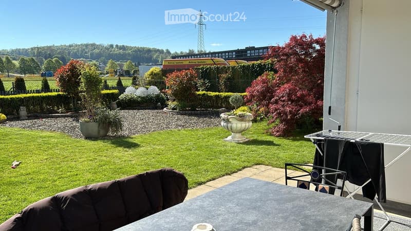 Well-maintained garden with a lawn, potted plants, a decorative urn, and a patio area with a table and chairs.
