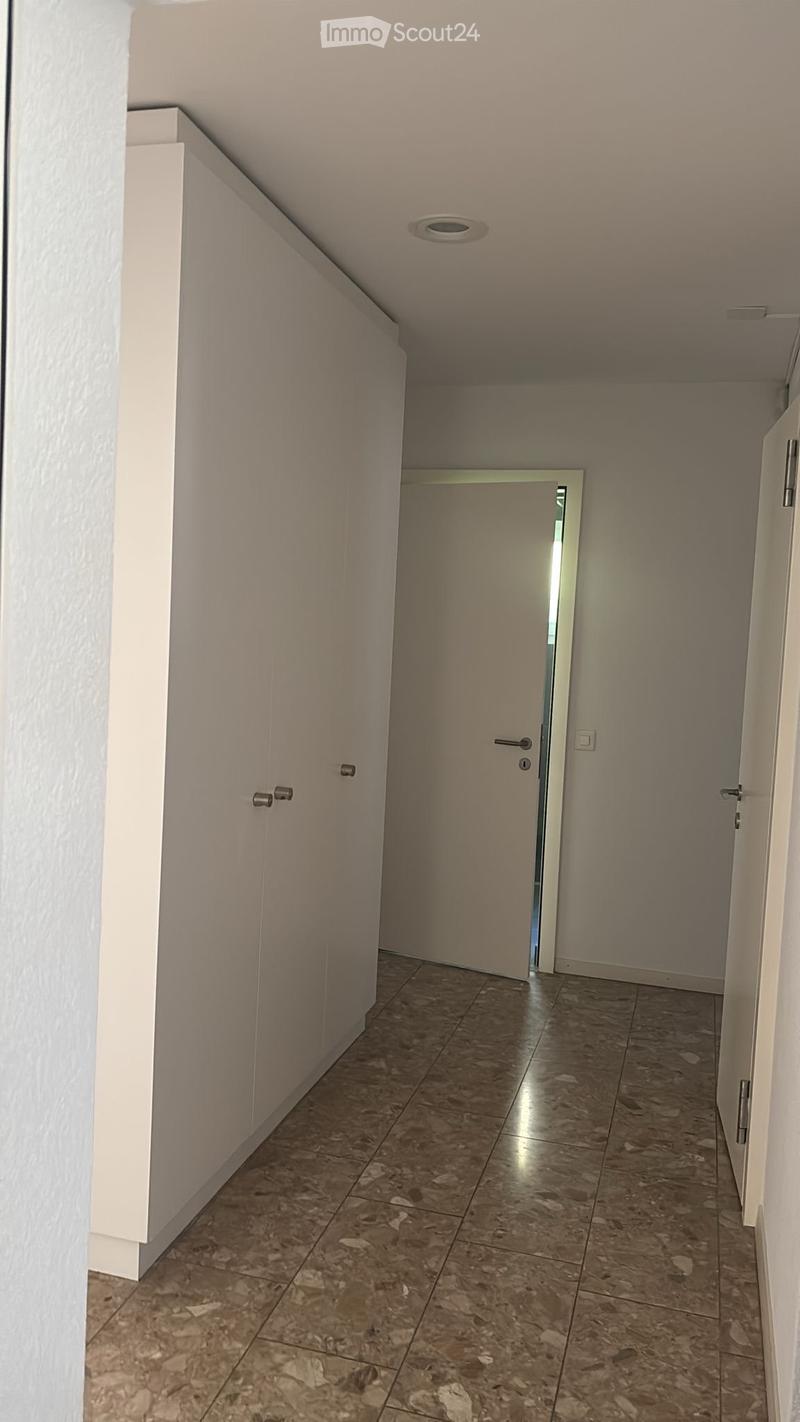 Empty hallway with tiled floor, white walls, and a closed door at the end.