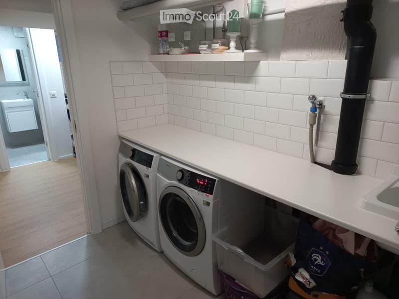 Clean bathroom with white tiled walls, a washing machine, a sink, and a towel hanging on the wall.