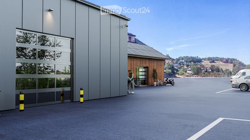 Modern industrial-style building with large garage doors, adjacent wooden structure, and parking area with several vehicles.