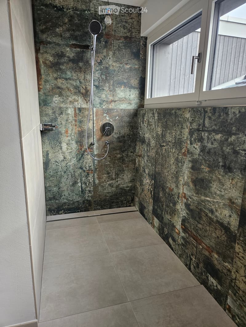 Modern shower area with marble-like tiles, a handheld showerhead, and a window with a white frame.