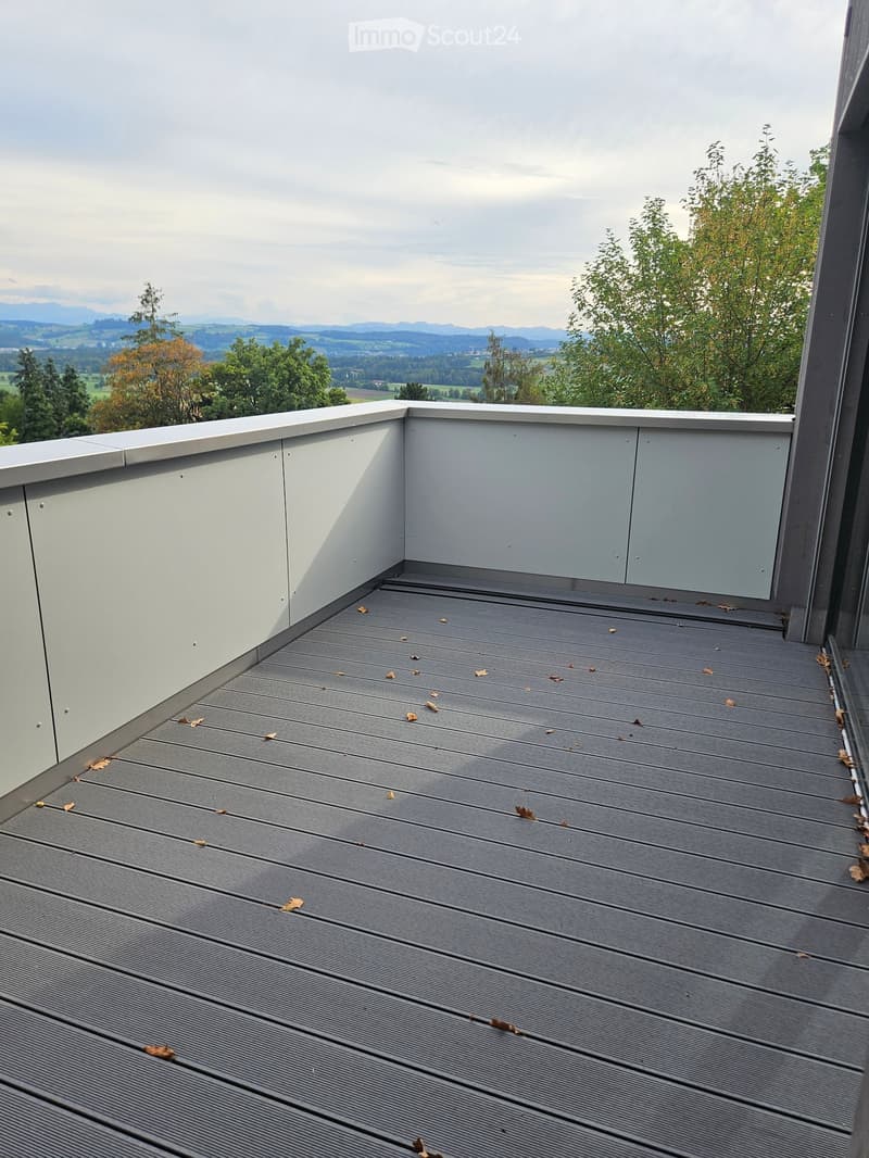 Modern grey wooden deck with low white railing, overlooking a scenic valley and distant mountains.