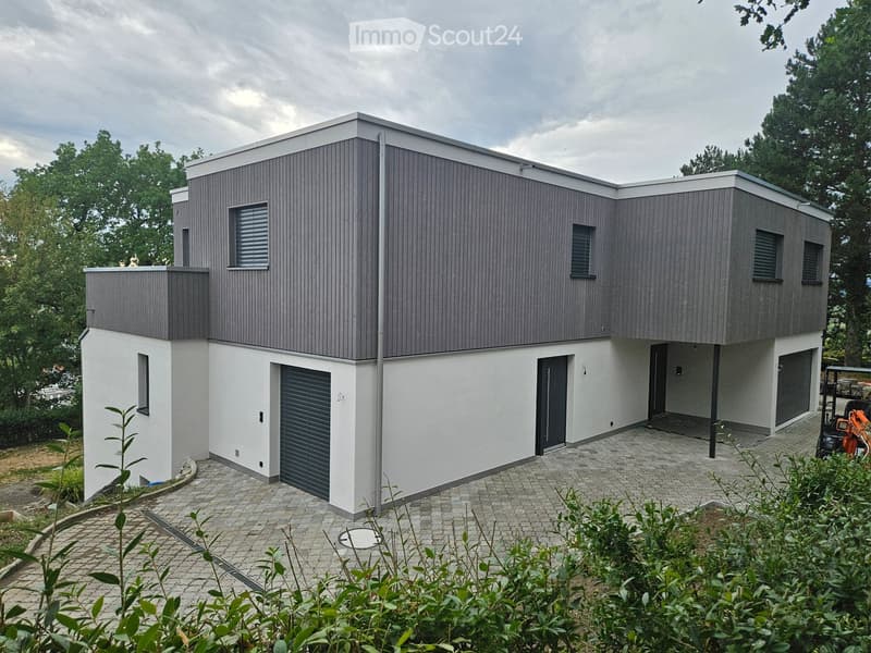 Modern two-story house with grey and white exterior, featuring a garage and multiple windows.
