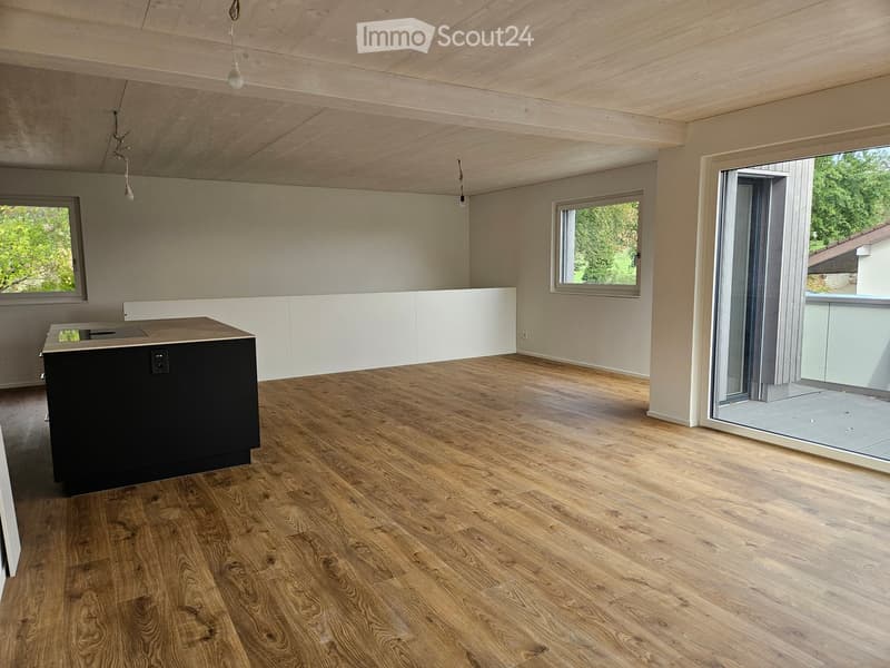 Open-plan kitchen with wooden flooring, white cabinetry, and a black kitchen island. Large windows and a sliding glass door lead to a balcony.