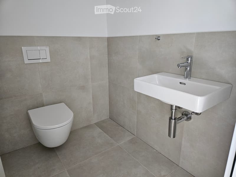 Modern bathroom with a toilet, sink, and faucet, featuring light grey tiled walls and floor.