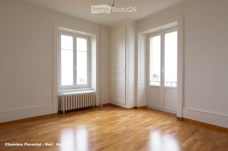 Empty room with wooden flooring, white walls, two windows, a radiator, and a white door.