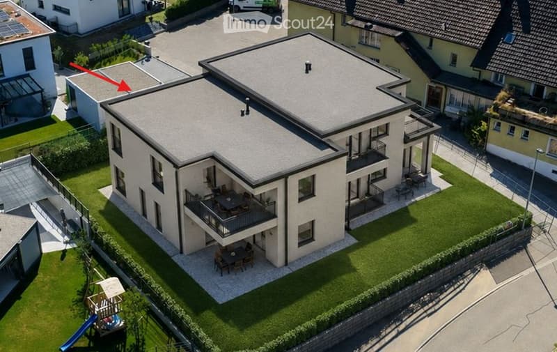 A modern two-story house with a flat roof, surrounded by a well-maintained lawn and neighboring houses. Features include balconies, outdoor seating areas, and a small playground.