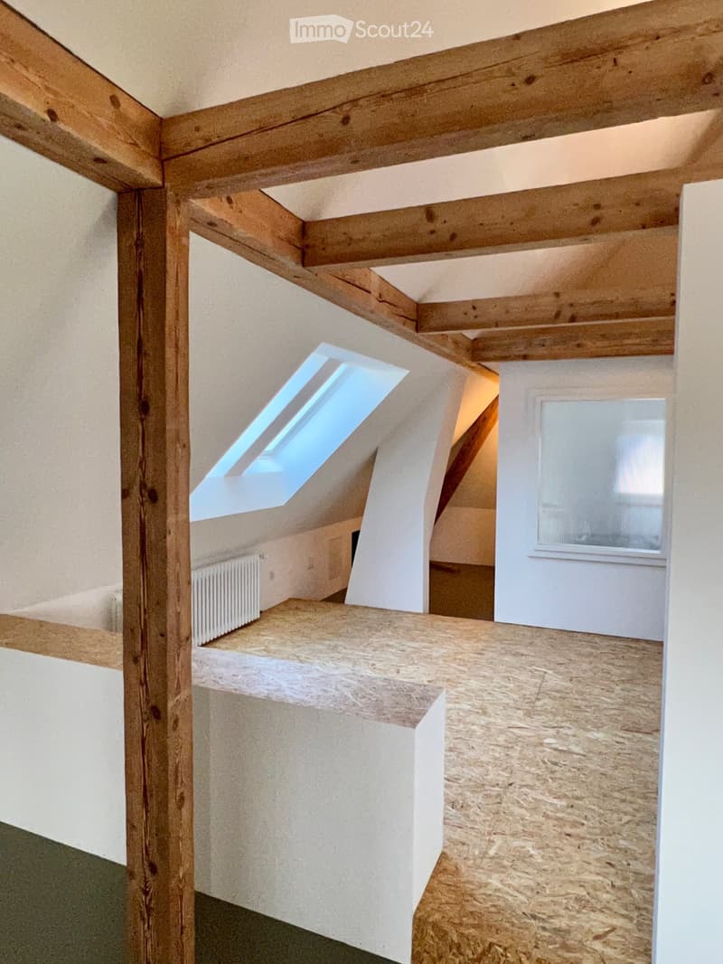 Empty attic space with exposed wooden beams, skylight window, and wooden floorboards.