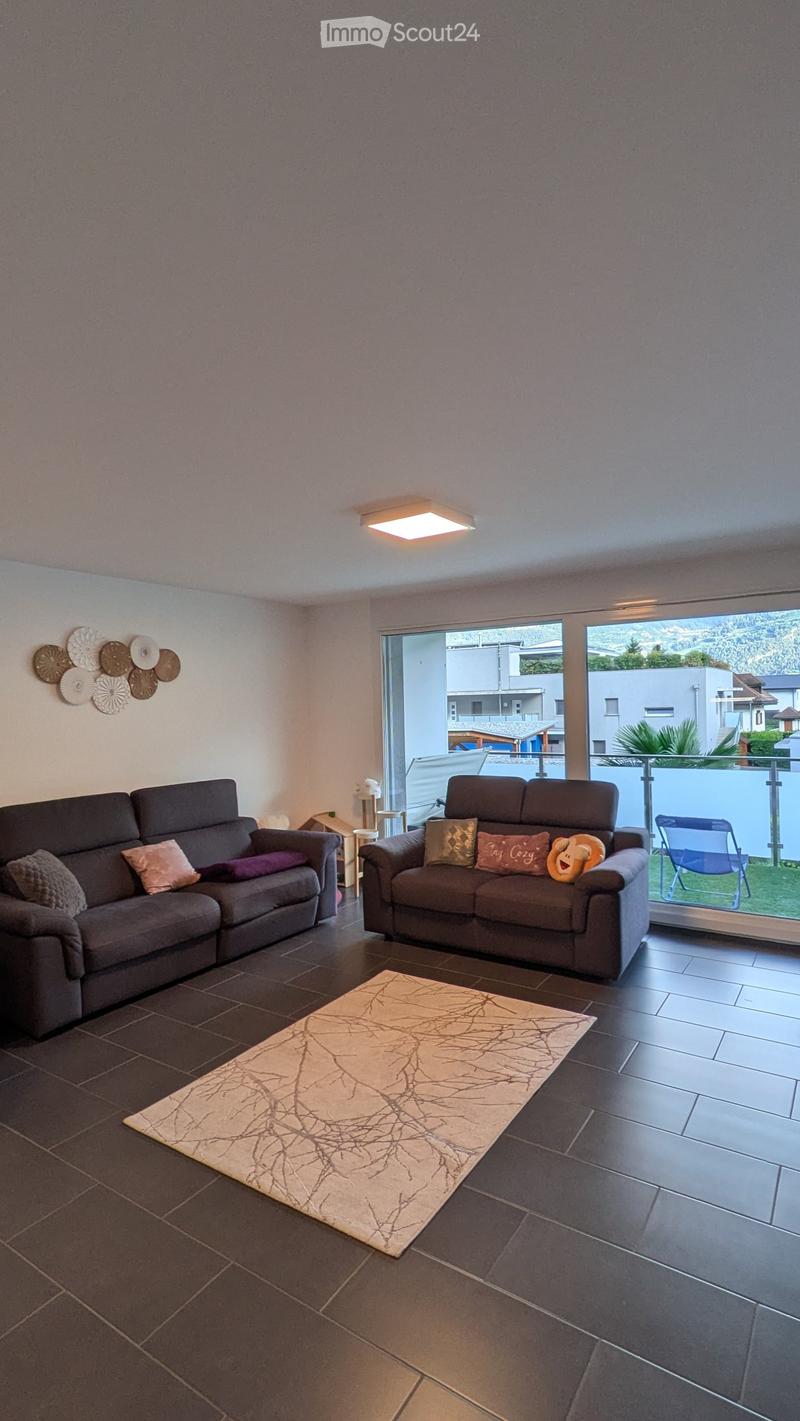Modern living room with two grey sofas, a beige rug, a small table, and a view of the outdoor area through large windows.