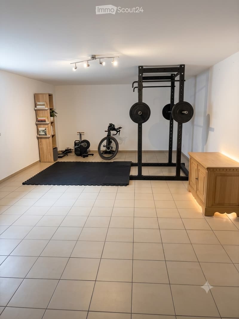Well-lit room with tiled floor, weight rack with weights, exercise bike, small stool, bookshelf, and wooden cabinet.