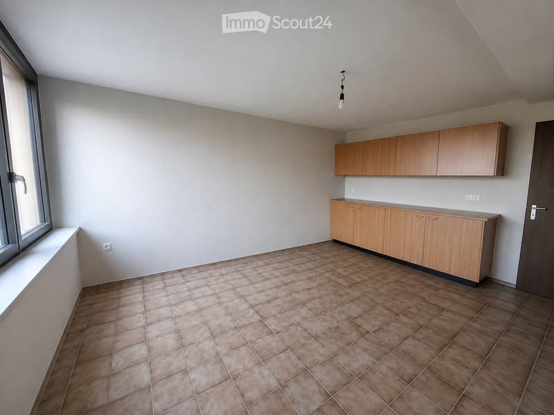 Empty room with tiled floor, light wooden cabinets, and a large window with a white sill.