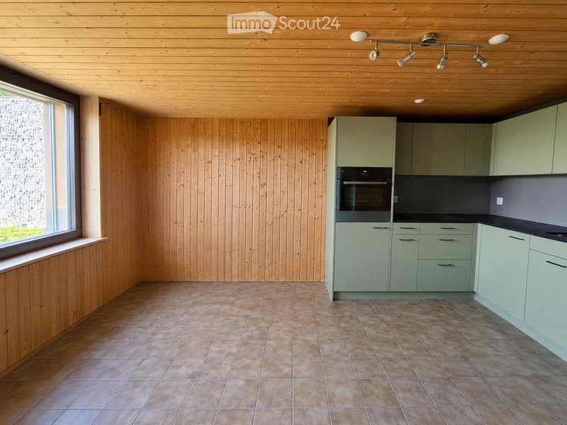 Modern kitchen with light green cabinets, wooden walls, tiled floor, and built-in oven.