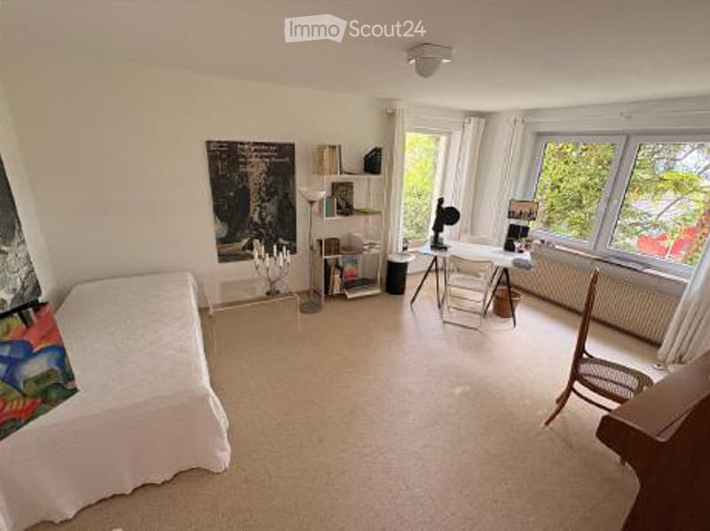 A well-lit room with a bed, a chair, a table, a shelf, a lamp, and a picture frame on the wall.
