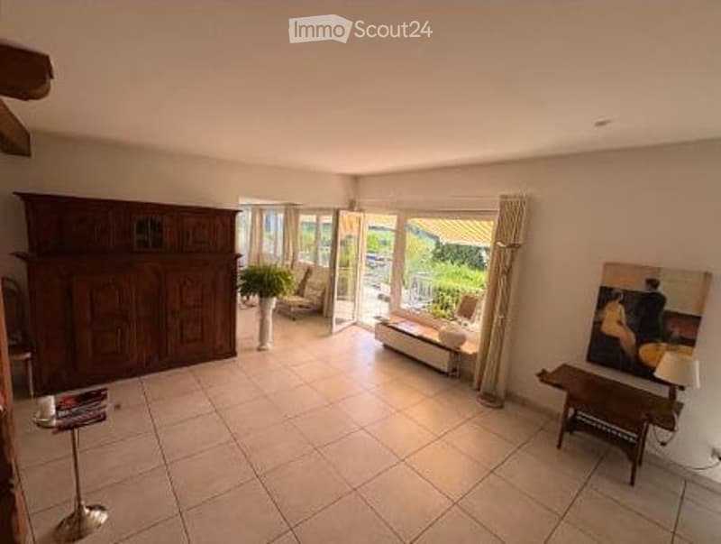 Bright living room with large sliding glass doors leading to a balcony, featuring a sofa, coffee table, chairs, a wooden cabinet, and a floor lamp.