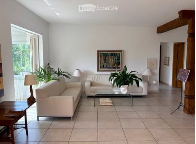 Bright living room with white walls, tiled floor, cream-colored sofa, coffee table, table lamps, and potted plants.