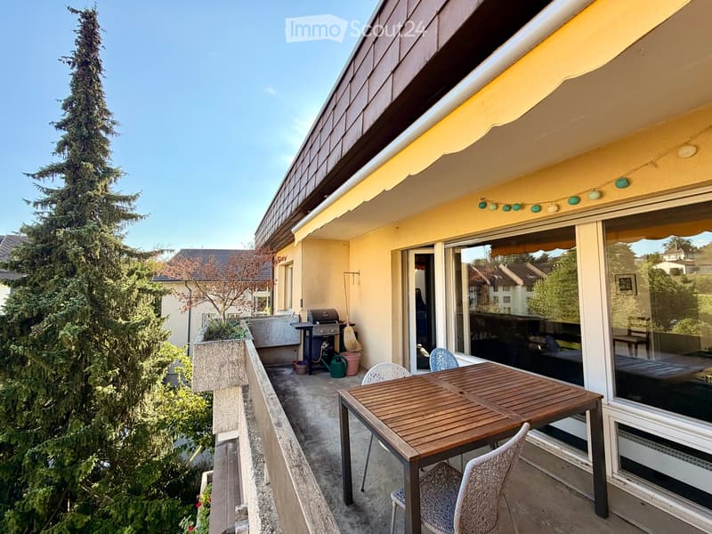 Balcony with a wooden table, chairs, grill, and outdoor plants.