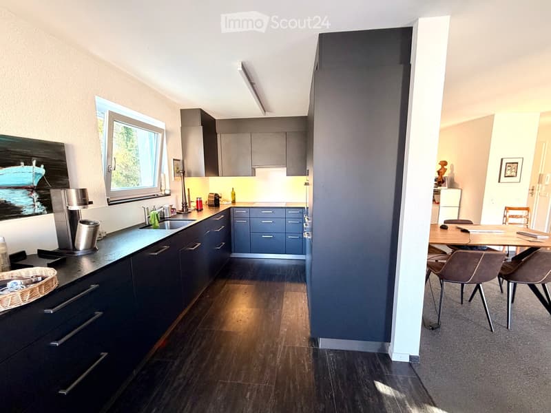 Modern kitchen with dark blue cabinets, stainless steel appliances, and a dining area with a wooden table and chairs.