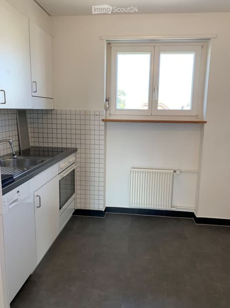 Modern kitchen with white cabinets, dark countertops, a sink, an oven, and a radiator under a window.