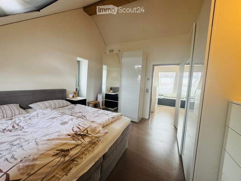 Bedroom with a large bed, nightstand, mirror wardrobe, and a view of a bathroom through an open doorway.