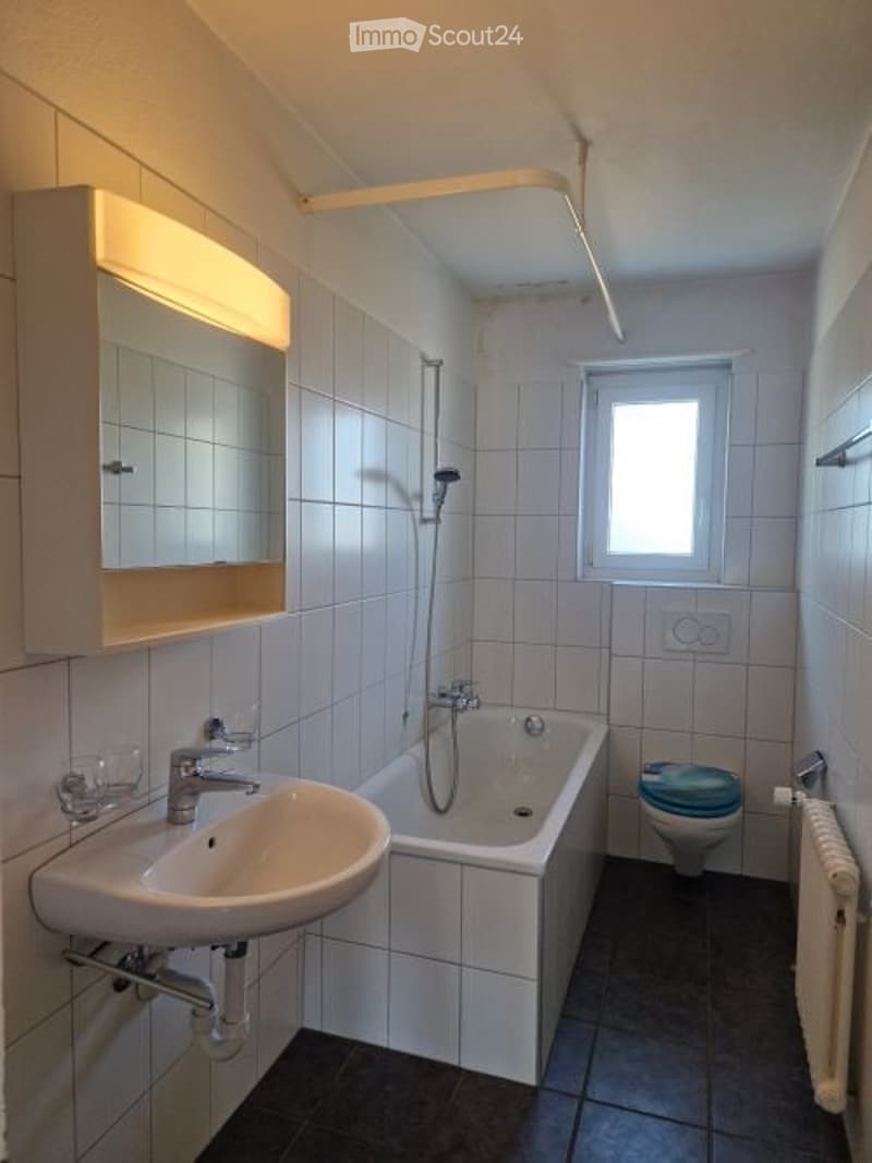 Modern bathroom with white tiles, a sink, bathtub, toilet, mirror, and a radiator.