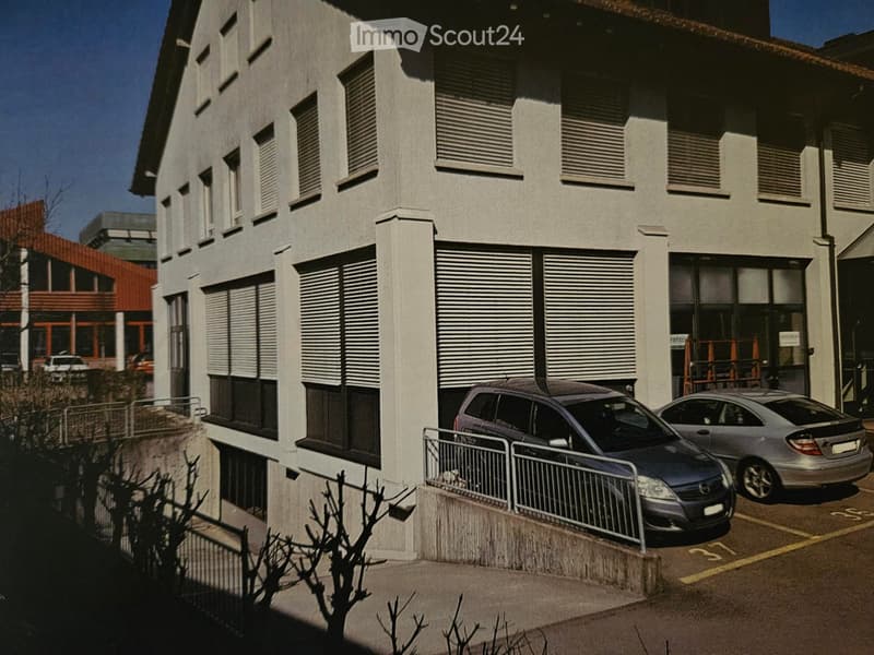 Modern multi-story building with grey facade, large windows, and a parked car in front.