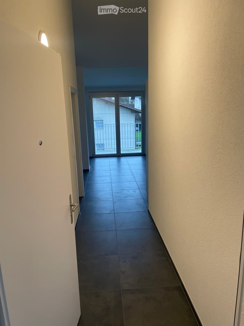 A narrow hallway with tiled flooring, white walls, and a sliding glass door leading to an outdoor area.
