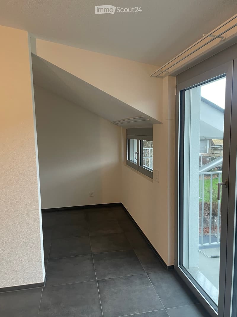 Empty hallway with dark tiled floor, light-colored walls, and a large window at the end leading to a balcony area.