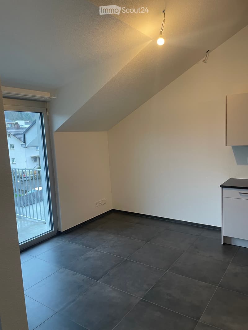 Empty room with dark tiled floor, white walls, and a sliding glass door leading to a balcony. A small white cabinet is visible on the right side.