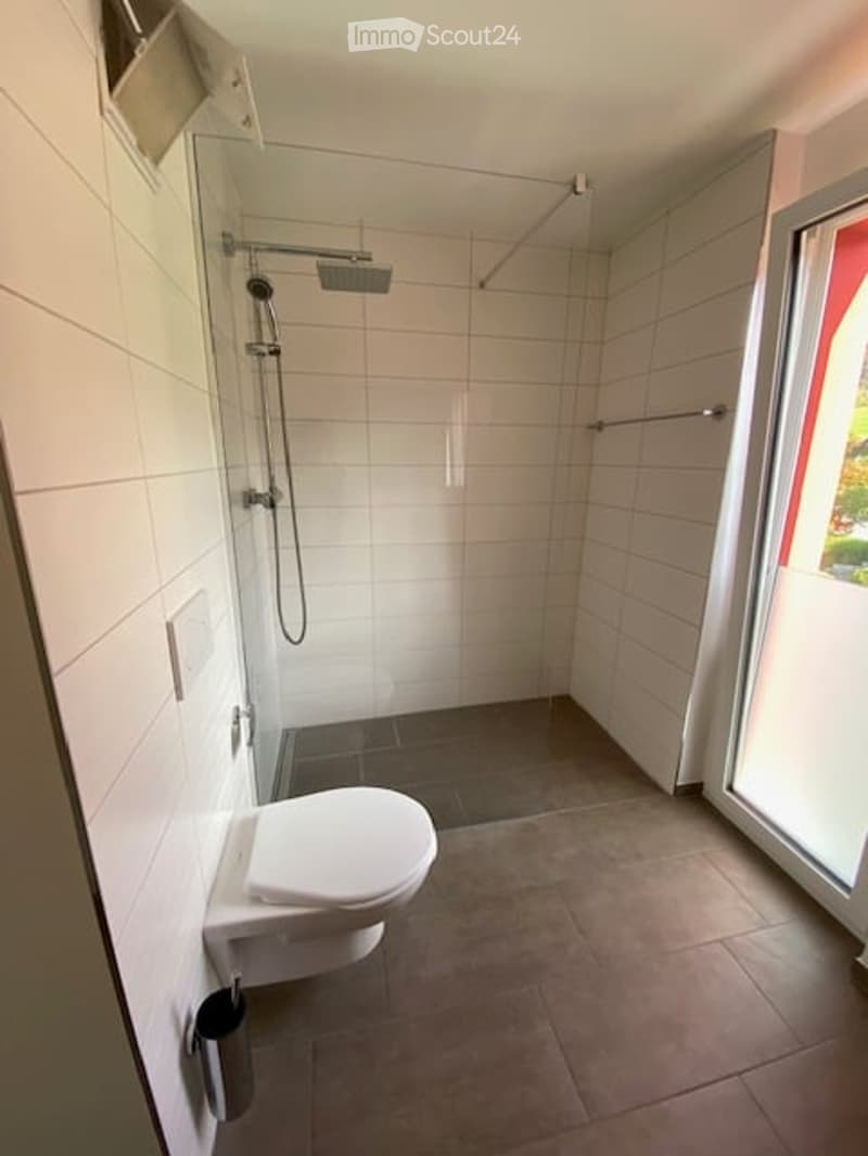 Modern bathroom with white tiled walls, a toilet, a shower with a handheld showerhead, and a towel rack.