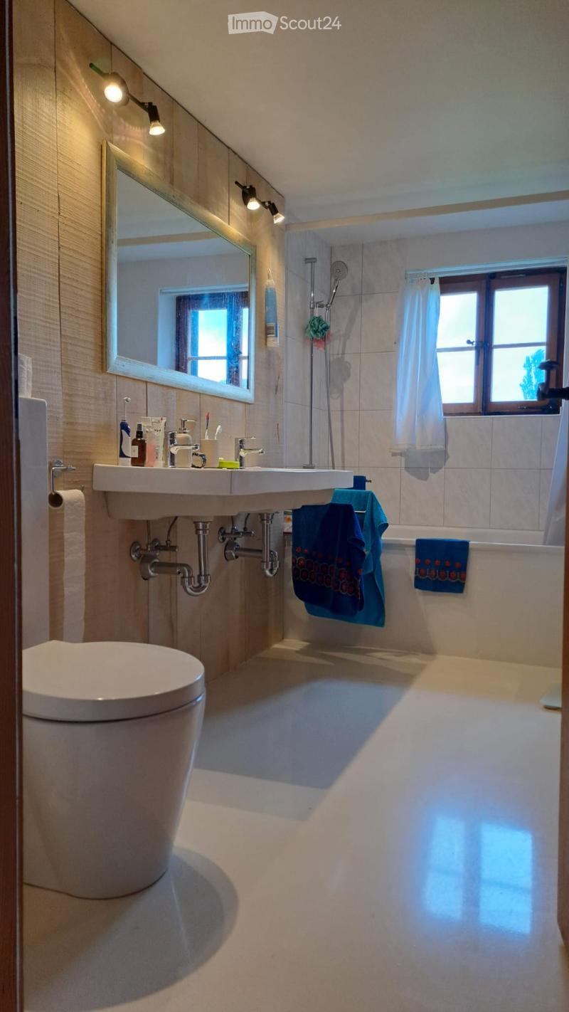 Modern bathroom with a toilet, double sink, bathtub, large mirror, and blue towels hanging on the side.