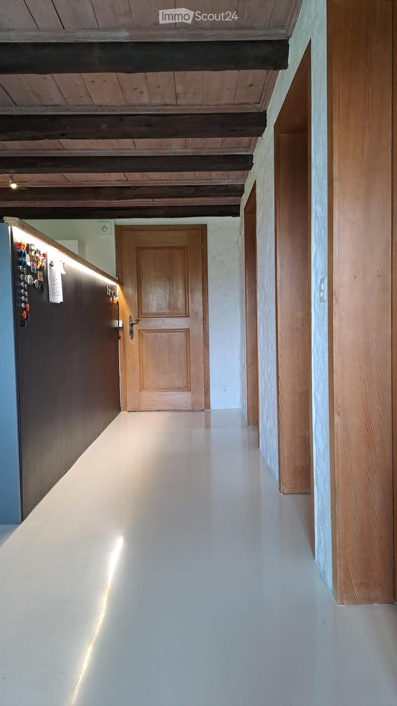 A long, narrow hallway with wooden doors and a polished white floor, featuring exposed wooden beams on the ceiling and recessed lighting.