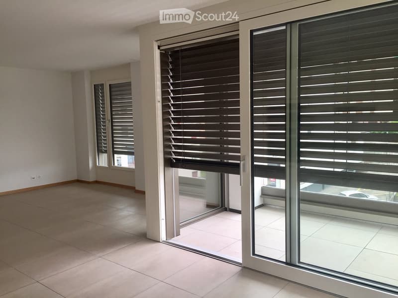 Empty room with tiled floor, large windows with blinds, and a sliding glass door leading to a balcony area.