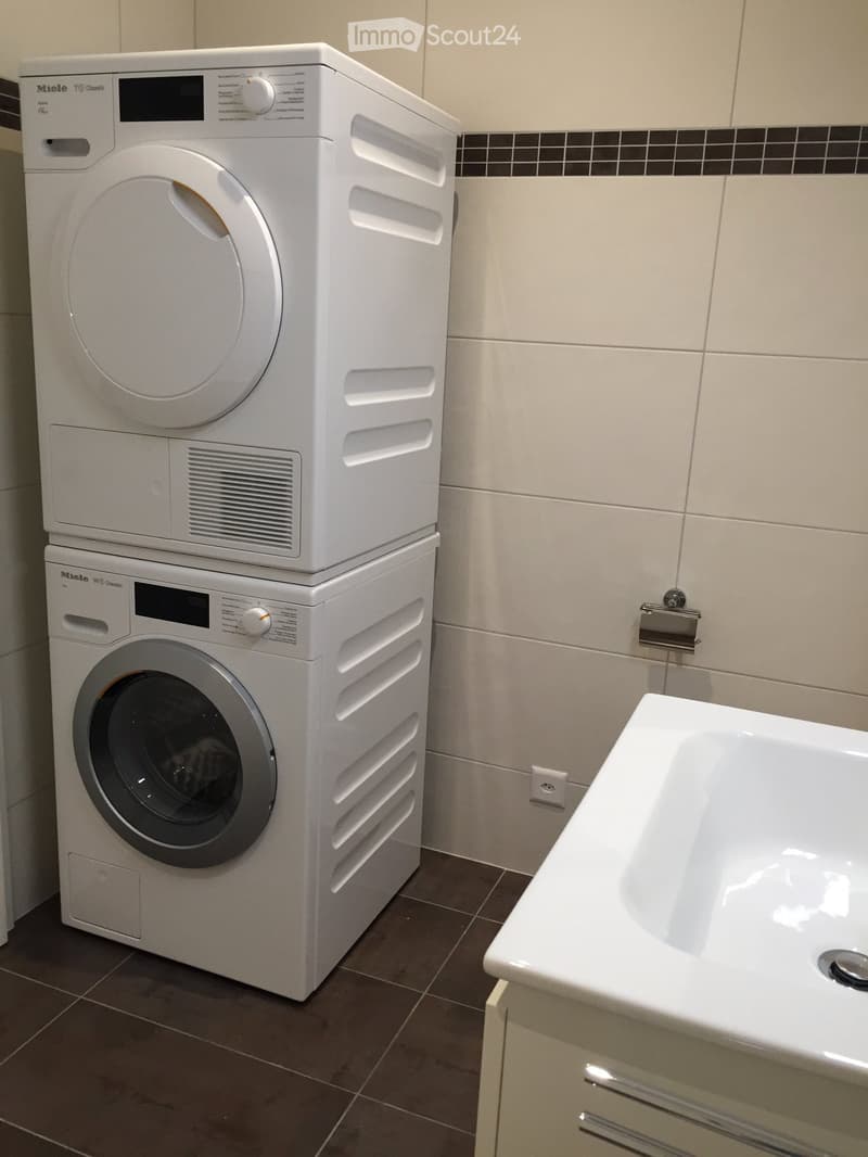 Bathroom with a white washing machine and dryer stacked, a white bathtub, and a cabinet.