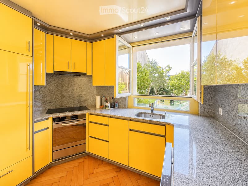 Modern kitchen with bright yellow cabinets, granite countertops, and wooden flooring. Features a sink, oven, and various small items on the counter.
