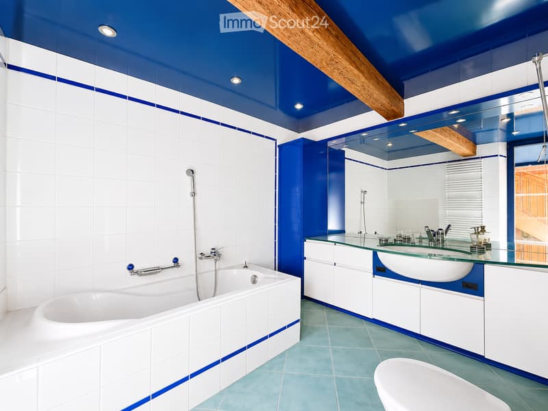 Modern bathroom with white and blue tiles, a bathtub, a sink with a mirror, and a glass countertop.