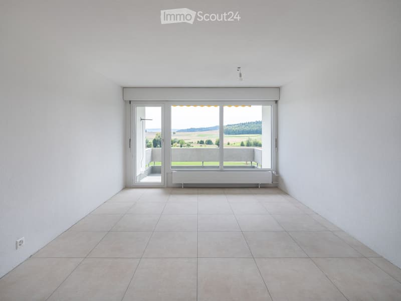 Empty room with white walls, tiled floor, large windows, and a radiator. No furniture or equipment present.