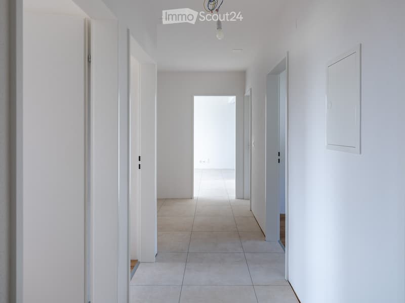 A clean, modern hallway with white walls, tiled floor, and several open doors leading to other rooms.