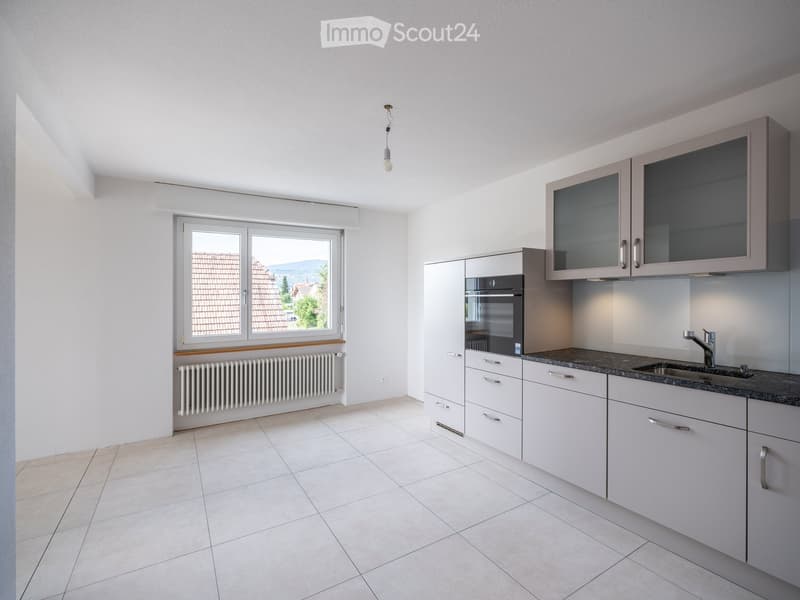 Modern kitchen with white cabinets, granite countertop, stainless steel sink, and built-in oven. Large window with view of roofed area and landscape.