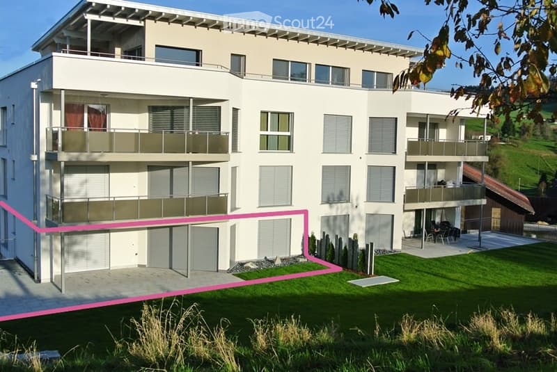 Modern two-story building with multiple balconies, large windows, and a well-maintained lawn in front.