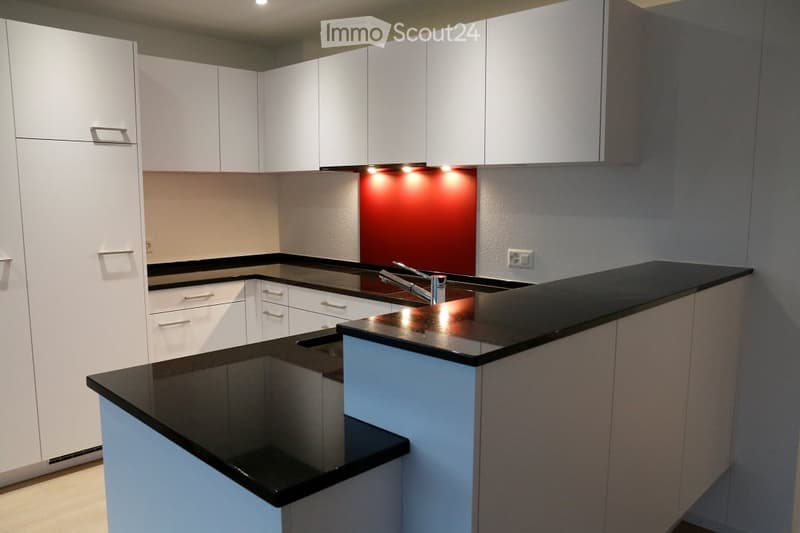 Modern kitchen with white cabinets, black countertops, and a central island. Features a sleek design with built-in lighting and a stainless steel faucet.