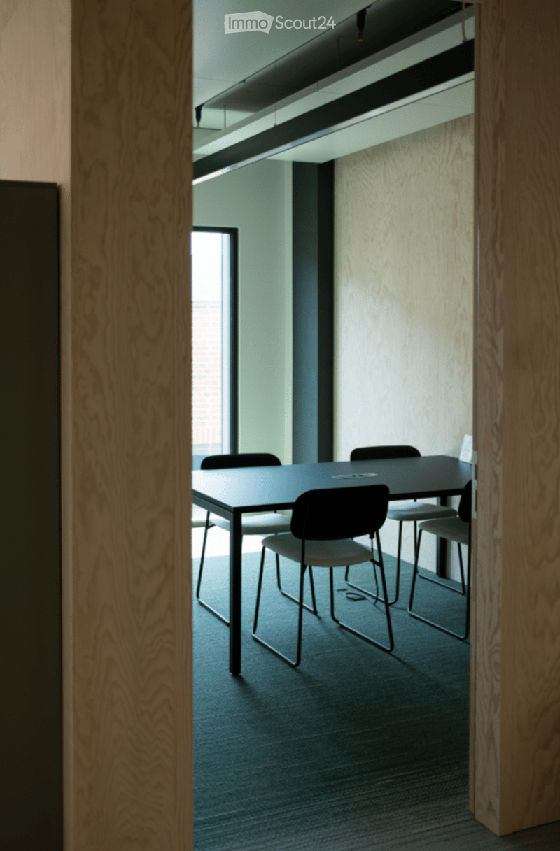 Modern meeting room with a sleek black table and several chairs, wooden panel walls, and large windows allowing natural light.