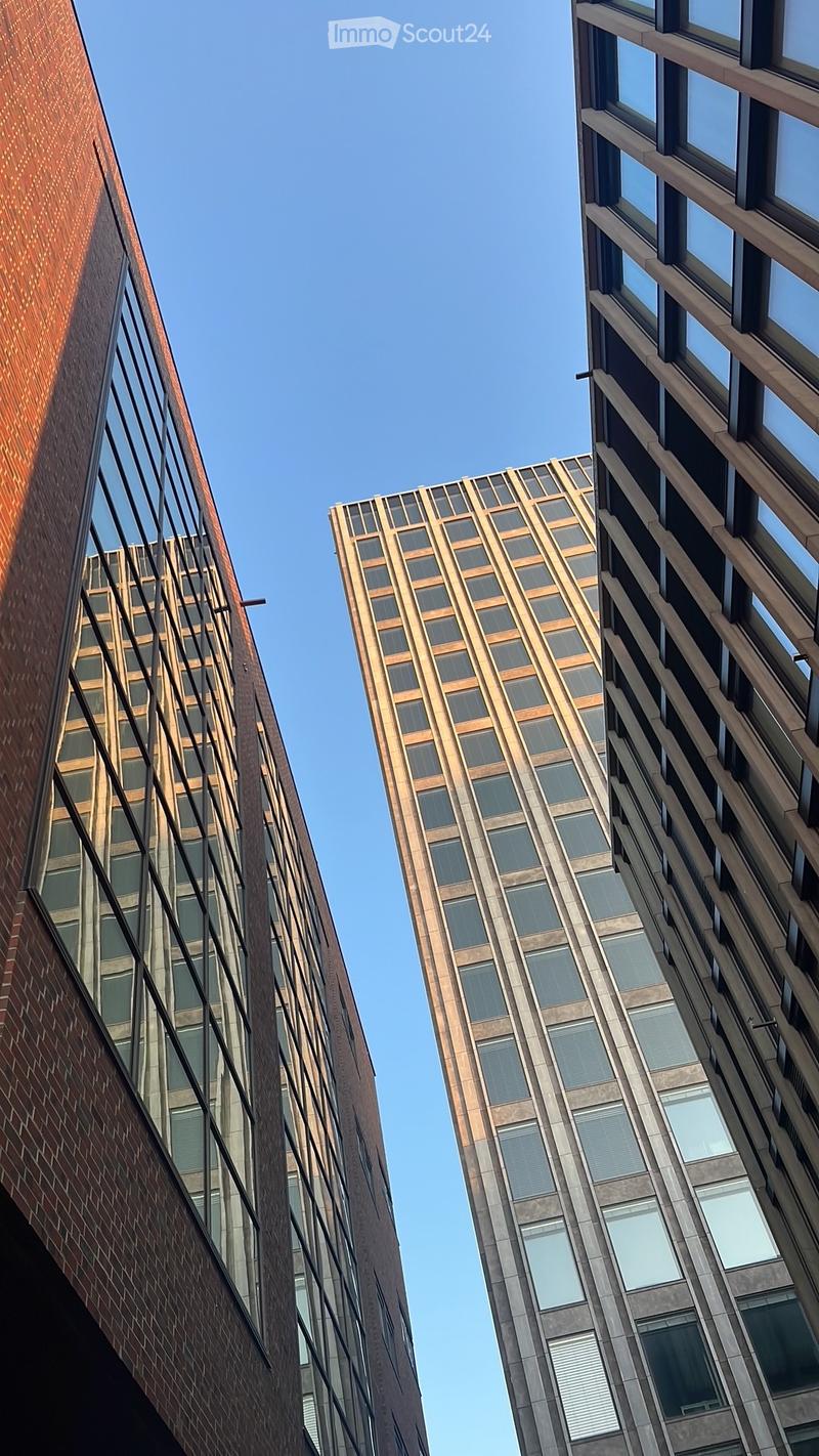 Modern high-rise buildings with glass windows and metal facades, set against a clear blue sky.
