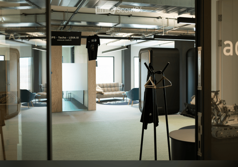 Modern office space with a sofa, chairs, small tables, and a coat rack with a coat hanging on it.