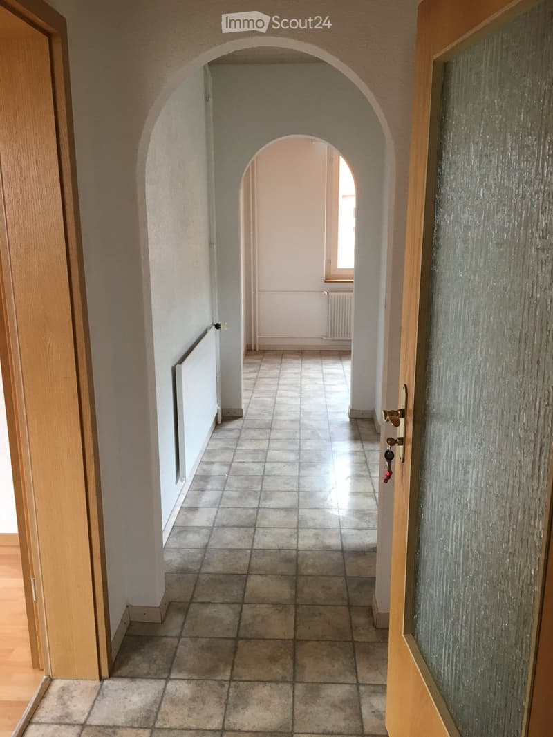 Empty hallway with tiled floor, arched doorways, and light-colored walls.