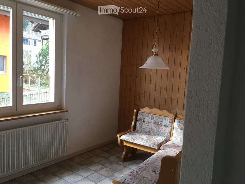 Cozy room with wooden walls, tiled floor, and a window offering a view of the outside. Features a patterned sofa and a radiator below the window.